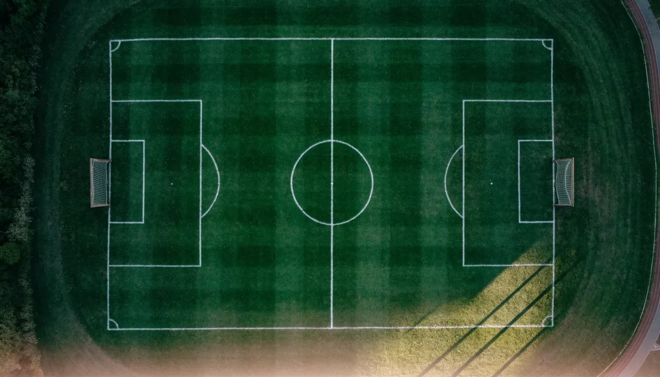Ein Fussballplatz von oben gesehen, die Linien bilden ein helles Muster auf dem Rasen, Drohnenperspektive in der Morgendämmerung.