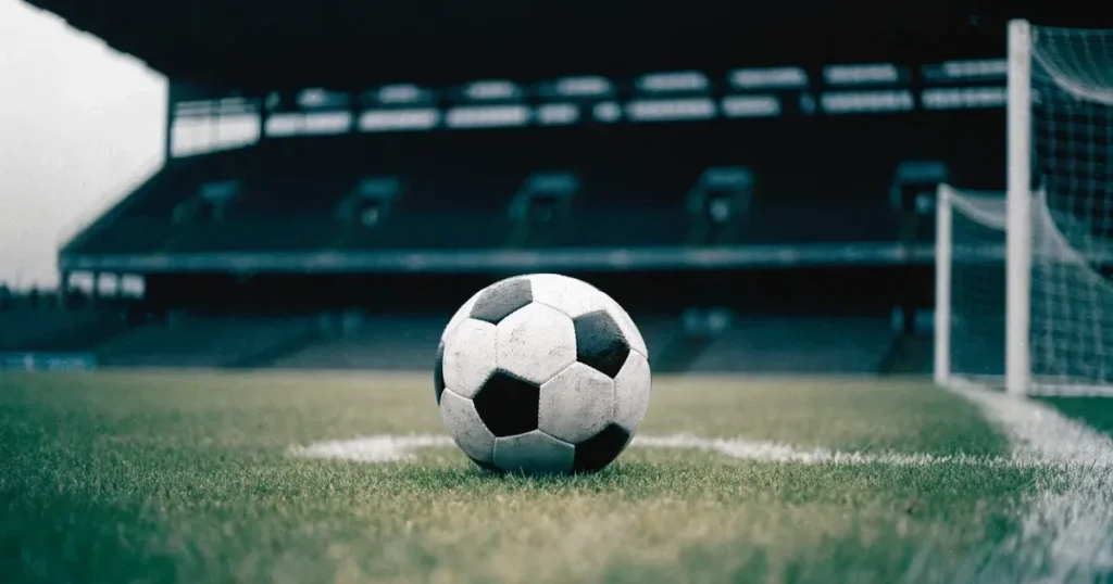 Ein Fussball liegt auf dem Anstosspunkt eines frisch gemähten Rasens, dahinter eine grosse Tribüne unter bewölktem Himmel