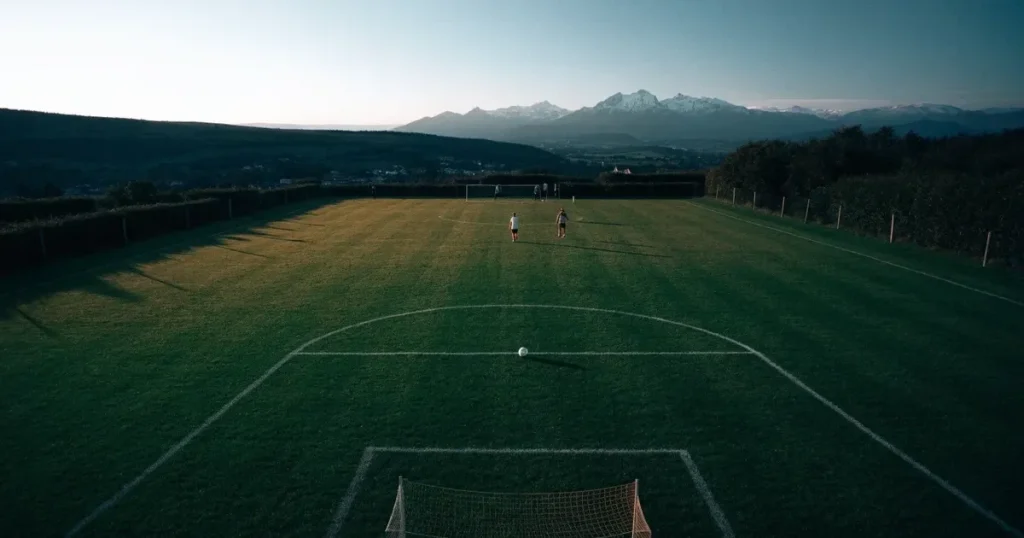 Ein Fussballplatz aus der Vogelperspektive mit sauberen Linien auf dichtem Rasen, in der Ferne verschneite Berge.