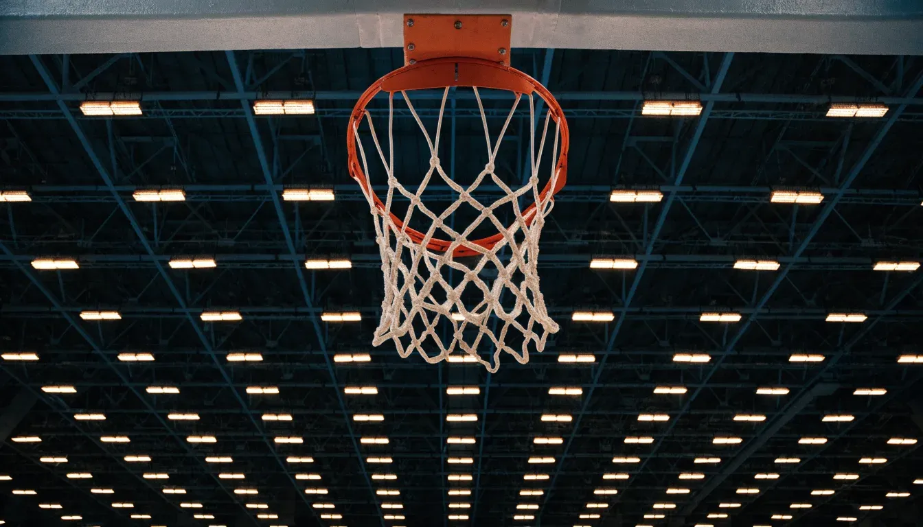 Ein Basketballkorb von unten gesehen, darüber eine Hallendecke mit Scheinwerfern und Stahlträgern.