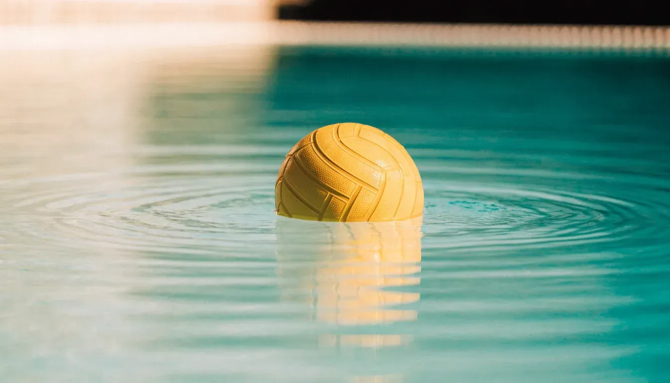 Ein gelber Ball treibt auf ruhigem türkisfarbenem Beckenwasser, feine Wellen im weichen Licht.